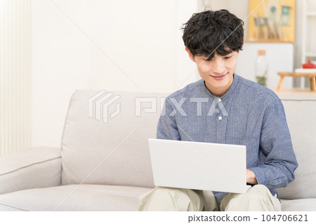 Young man sitting on a sofa and using a laptop on his lap 104706621