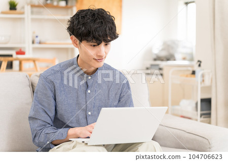 Young man sitting on a sofa and using a laptop on his lap 104706623