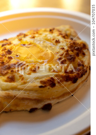 Traditional Georgian cuisine. Ajara khachapuri on paper plate. Filled with cheese and topped with raw egg and butter, cheese-filled bread Traditional Georgian cuisine. Ajara khachapuri on paper plate. Filled with cheese and topped with raw egg and butter, cheese-filled bread 104707035
