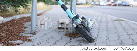 Locked electric kick scooter in urban street 104707169