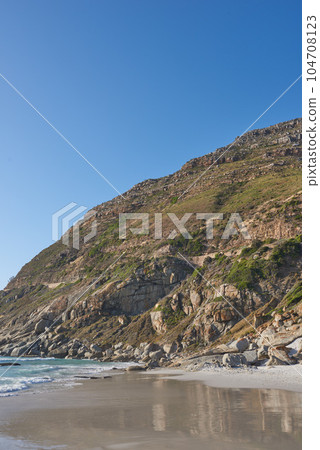 Beautiful view of a nature landscape with the sea, sand, and a blue sky background. Natural outdoors setting of the beach and green mountains. Isolated environment outside near ocean water. Beautiful view of a nature landscape with the sea, sand, and a blue sky background. Natural outdoors setting of the beach and green mountains. Isolated environment outside near ocean water. 104708123
