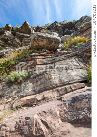 Rocky mountain with big boulders for outdoor climbing while on nature adventure during summer. Landscape of lush shrubs, green plants and rocks on a cliff with blue sky in the background 104708232