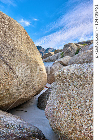 Rocky coast. Big rocks on the beach with a blue sky background on a summer day. A landscape of large or huge boulders on the ocean shore of a remote location. Seaside with huge stones on the sand. Rocky coast. Big rocks on the beach with a blue sky background on a summer day. A landscape of large or huge boulders on the ocean shore of a remote location. Seaside with huge stones on the sand. 104708451