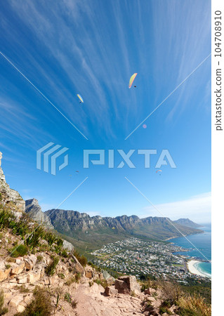 People paragliding from a mountain with a scenic view in summer. Tourists having fun and doing adventurous activities while on holiday in a clear blue sky. People hand gliding from a cliff in nature 104708910