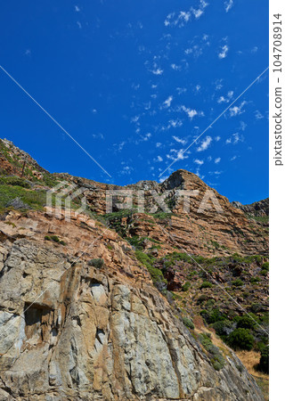 Scenic landscape of mountains against a blue sky background with scattered clouds and copy space from below. Wild plants and shrubs growing on rocky hill and cliff in a remote and natural environment 104708914