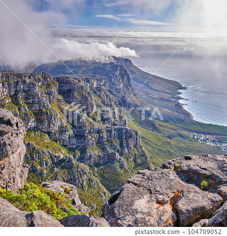 Panoramic aerial nature views of clouds rolling over a mountain on the coast during summer. Copyspace scenic view of a natural environment on a coastline with rocks, plants, and greenery from above Panoramic aerial nature views of clouds rolling over a mountain on the coast during summer. Copyspace scenic view of a natural environment on a coastline with rocks, plants, and greenery from above 104709052