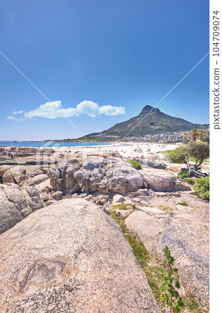 Large rocks at a beach near a mountain with a blue sky background on a hot summer day. The landscape of a rocky sea or ocean shore during spring break. Sunny coastal land with large stones 104709074