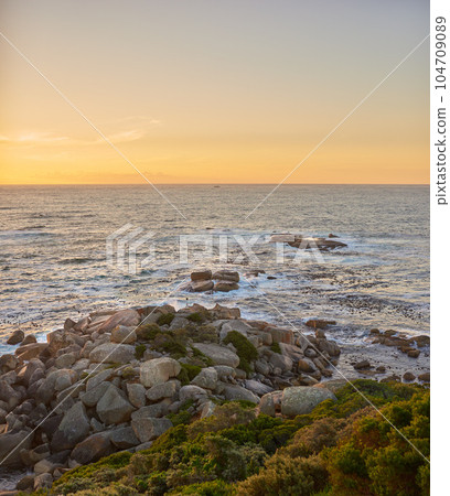 Copyspace landscape of an ocean view against a sunset sky in summer. Beautiful and calm scenery from the beach seaside while the sun sets in the distance. Natural environment of the sea at dawn 104709089