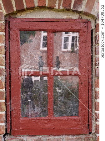 Closeup of an old dirty window in a red brick home. Zoom in on casement with red wood frame on a historic building with bumpy paint texture. Macro exterior details of windowsill in a traditional town Closeup of an old dirty window in a red brick home. Zoom in on casement with red wood frame on a historic building with bumpy paint texture. Macro exterior details of windowsill in a traditional town 104709352