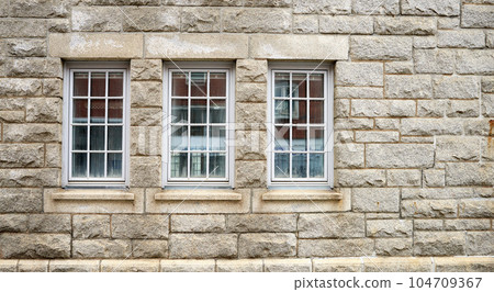 Old windows on the side of a brown stone building for architectural detail. Closeup of the cultural and textured design on a brick wall outside of a house, school or church in a small town Old windows on the side of a brown stone building for architectural detail. Closeup of the cultural and textured design on a brick wall outside of a house, school or church in a small town 104709367