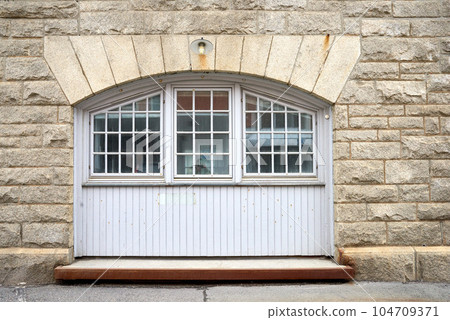 Oldwindow. Architecture of an old window in a brick wall. Facade of vintage white or classic windows on a house. Exterior details of a traditional, rustic residential building with light stone walls. Oldwindow. Architecture of an old window in a brick wall. Facade of vintage white or classic windows on a house. Exterior details of a traditional, rustic residential building with light stone walls. 104709371