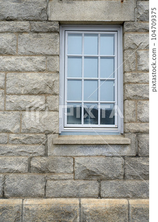 Shiny window and architecture of a grey brick wall. Exterior texture details of an old rustic residential building or private home with modern wooden windows and windowsill in a town or village Shiny window and architecture of a grey brick wall. Exterior texture details of an old rustic residential building or private home with modern wooden windows and windowsill in a town or village 104709375