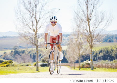 Fitness, countryside or man cycling on a bicycle for training, cardio workout and exercise outdoors alone. Wellness, healthy or sports athlete riding a bike on a road or path for freedom or challenge 104710029
