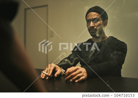 Man in investigation, smoking and detective in interrogation room with criminal, suspect or interview with a gangster. Police officer, questioning and statement of truth and person with cigarette 104710153
