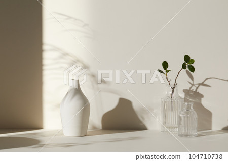 A room with various objects such as warm sunlight, shadows of grass leaves, a vase on a table, and cups 104710738