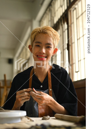 Delighted asian man kneading clay for creating pottery ceramics. Handicraft, creativity and hobby concept 104712529