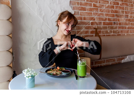 A girl in a cafe at breakfast shows various gestures with her hands A girl in a cafe at breakfast shows various gestures with her hands 104713108