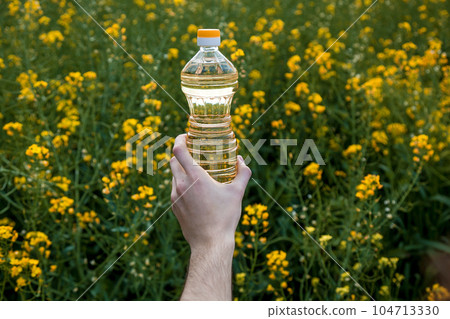 A man's hand holds a bottle of rapeseed oil 104713330