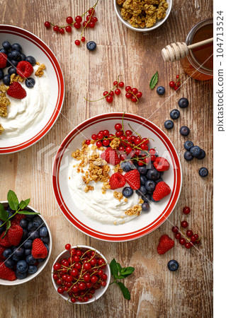 Yogurt with berries on wooden background. White plain greek yogurt with fresh berries and granola, top view. Healthy food, breakfast menu Yogurt with berries on wooden background. White plain greek yogurt with fresh berries and granola, top view. Healthy food, breakfast menu 104713524