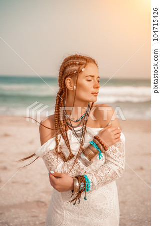 Woman portret sea white dress. Model in boho style in a white long dress and silver jewelry on the beach. Her hair is braided, and there are many bracelets on her arms. Woman portret sea white dress. Model in boho style in a white long dress and silver jewelry on the beach. Her hair is braided, and there are many bracelets on her arms. 104715426