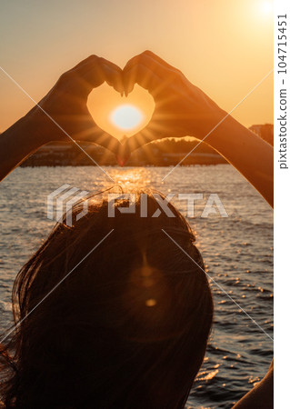 Silhouette against the sunset - hands folded in the shape of a h 104715451