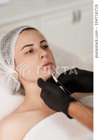 cosmetologist marking skin of caucasian woman with pencil. cosmetologist marking skin of caucasian woman with pencil. 104716719
