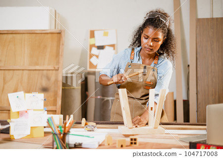 African black woman carpenter joiner working build wooden chair handcraft furniture in wood studio workshop. African black woman carpenter joiner working build wooden chair handcraft furniture in wood studio workshop. 104717008