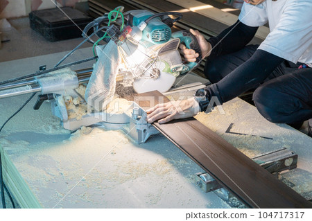 Carpenter cutting solid floorboards with slide saw 104717317