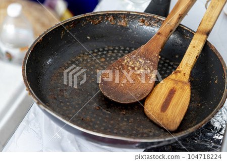 Empty black round cast iron pan with a spatula and a wooden spatula that had just finished cooking on the stove in the middle of the day Empty black round cast iron pan with a spatula and a wooden spatula that had just finished cooking on the stove in the middle of the day 104718224