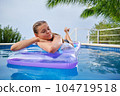 A young woman is relaxing by the pool. in the background a garden and palm trees. 104719518