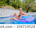 A young woman is relaxing by the pool. in the background a garden and palm trees. 104719528