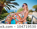 A young woman is relaxing by the pool. in the background a garden and palm trees. 104719530