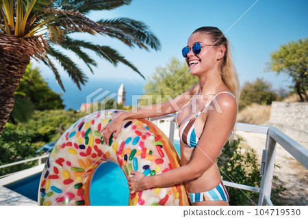 A young woman is relaxing by the pool. in the background a garden and palm trees. 104719530