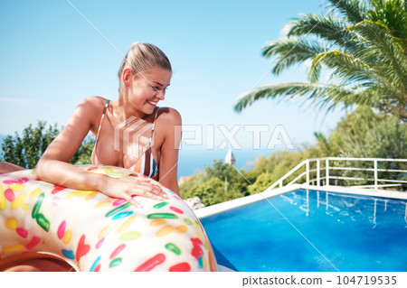 A young woman is relaxing by the pool. in the background a garden and palm trees. 104719535