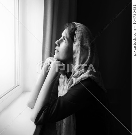 Girl praying by the window 104720481
