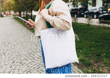 Close up of woman holding eco or reusable shopping bag and using smartphone outdoors. Urban lifestyle concept Close up of woman holding eco or reusable shopping bag and using smartphone outdoors. Urban lifestyle concept 104721317