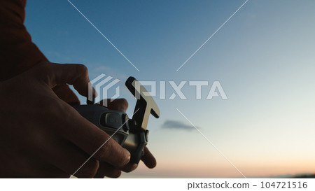 Silhouette of hand pilot of an fpv drone at sunset Silhouette of hand pilot of an fpv drone at sunset 104721516