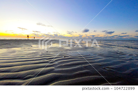 View of the setting sun shining on the Sea and reflected on the beach, clouds with sun-shining edges View of the setting sun shining on the Sea and reflected on the beach, clouds with sun-shining edges 104722899