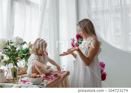 A little blonde girl with her mom on a kitchen countertop decorated with peonies. The concept of the relationship between mother and daughter. Spring atmosphere. A little blonde girl with her mom on a kitchen countertop decorated with peonies. The concept of the relationship between mother and daughter. Spring atmosphere. 104723274