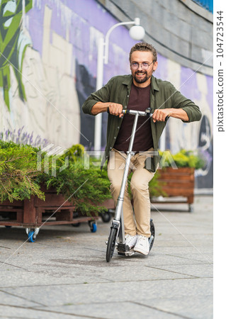 Man on a scooter performing stunts with a big wheel scooter. With a handsome and confident appearance, he showcases his skills and has a blast while engaging in thrilling maneuvers. High quality photo Man on a scooter performing stunts with a big wheel scooter. With a handsome and confident appearance, he showcases his skills and has a blast while engaging in thrilling maneuvers. High quality photo 104723544