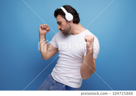 a cute young brutal brunette guy in white comes off to music in headphones a cute young brutal brunette guy in white comes off to music in headphones 104725888