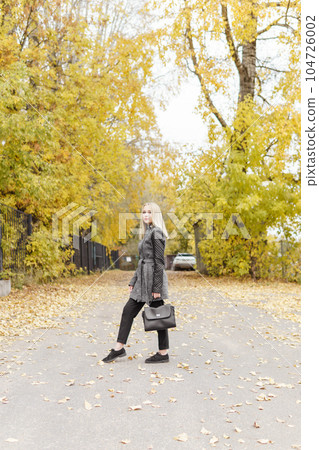 A young blonde walks through the autumn city in a gray coat. The concept of urban style and lifestyle. A young blonde walks through the autumn city in a gray coat. The concept of urban style and lifestyle. 104726002
