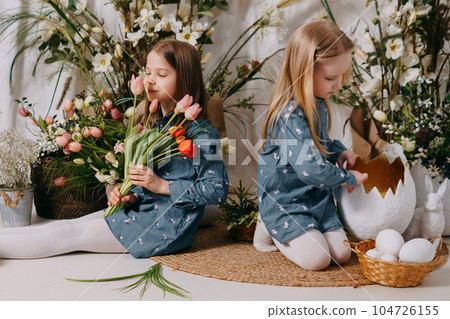 Two girls in a beautiful Easter photo zone with flowers, eggs, chickens and Easter bunnies. Happy Easter holiday. Two girls in a beautiful Easter photo zone with flowers, eggs, chickens and Easter bunnies. Happy Easter holiday. 104726155
