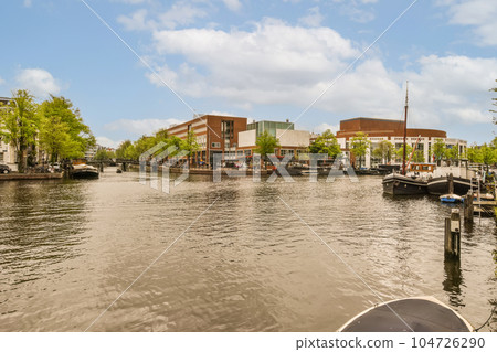 some boats in the water and buildings on the other side of the river, with blue sky above them all around 104726290