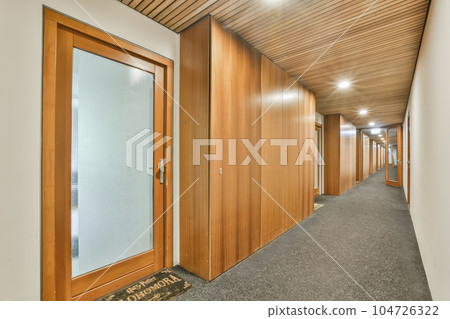 an office hallway with wood paneled walls and glass door leading to the first floor, which is lined with grey carpet an office hallway with wood paneled walls and glass door leading to the first floor, which is lined with grey carpet 104726322