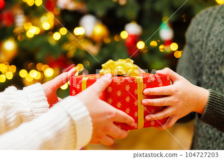 Hands of parent giving Christmas gift to child on Christmas tree background Hands of parent giving Christmas gift to child on Christmas tree background 104727203