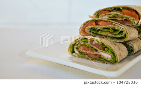 Salmon salad sandwich on a white plate. Roll lavash sandwich with red fish and lettuce. Thin mexican tortilla. Festive snack. 104728030