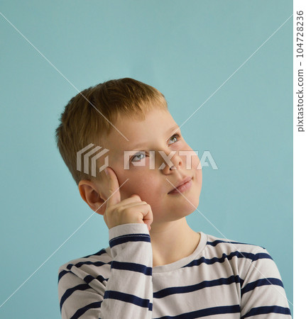 A white Caucasian boy in a striped jacket stands on a blue background, thinking. A white Caucasian boy in a striped jacket stands on a blue background, thinking. 104728236