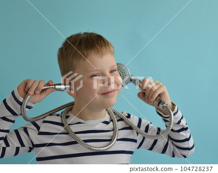 A happy smiling boy with a watering can from the shower on a blue background. The concept of housewarming, renovation, happy childhood. 104728237