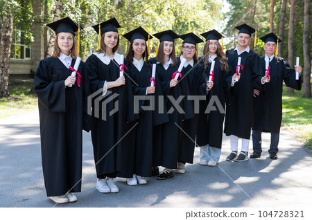 Row of young people in graduation gowns outdoors. Age student. 104728321